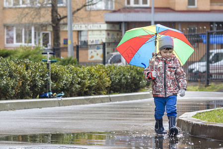 小男孩带着彩虹伞在下雨的公园玩耍图片