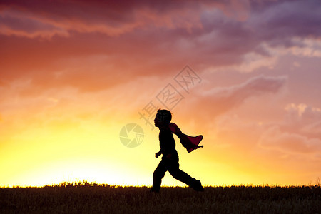 一个穿着斗篷的男孩在日落时高清图片