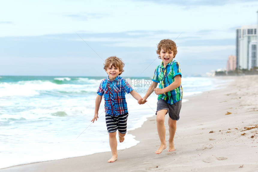 两个快乐的小孩男在海洋滩上奔跑有趣可爱的孩子兄弟姐妹和最好的朋友在风雨如磐的日子里度假户外玩图片