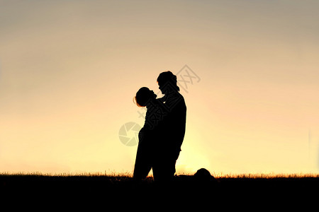 一个快乐的小男孩的轮廓在夏天日落时拥抱他父亲在外面的图片