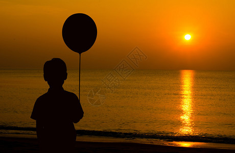 孤单的男孩拿着气球在海滩上看日落而等待他父母图片