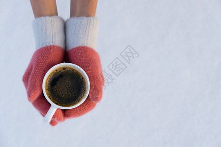 带着粉红色手套的女孩在雪中捧着一杯热咖啡图片