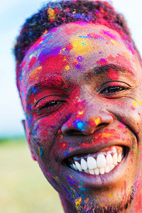 在霍利节的摄影机上微笑着脸涂着彩色脸颜料的非洲男图片