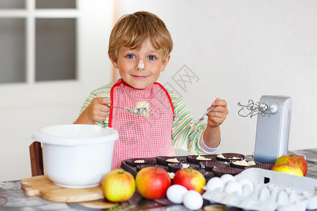 在家厨房里烤苹果蛋糕和松饼的男孩在与搅拌机面粉鸡蛋和水果一起工作时图片