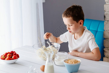 男孩在奶酪蛋糕碗中加糖和白奶酪图片