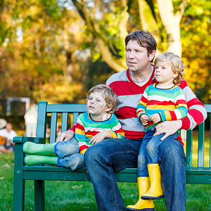年轻人和他的两个金发小儿子穿着多彩的衣服坐在一起图片