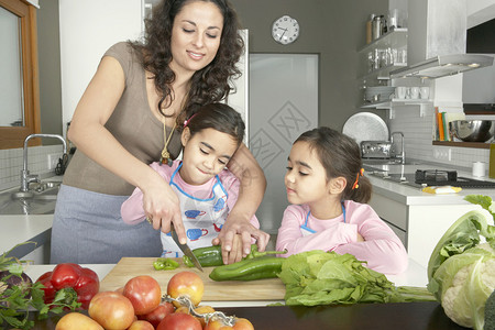 年轻母亲在一个家庭厨房里用双胞胎女儿切菜图片
