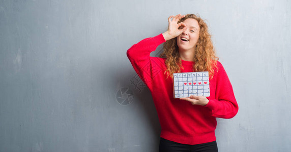 年轻的红发女人在灰色的格朗基墙上拿着周期日历图片