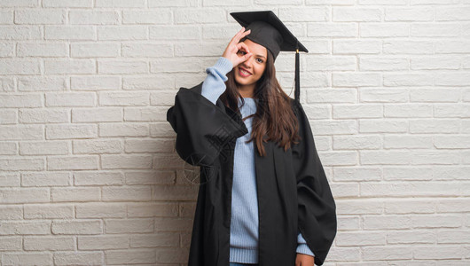 站在白砖墙上的黑发年轻女子穿着毕业制服图片