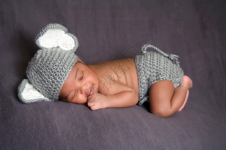 十三天大的微笑新生男婴戴着灰色钩编大象帽和尿布套他趴着睡在灰色背景