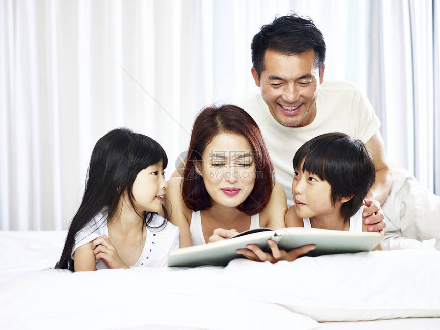 有两个孩子的亚洲家庭在家里床上看一本书图片