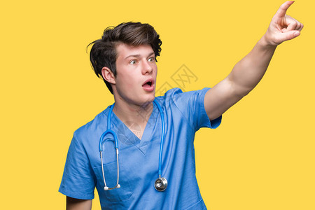 身穿医疗制服背景孤立的年轻医生用手指着前方图片