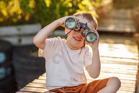 小男孩在河岸码头上看着双筒望远镜坐在图片