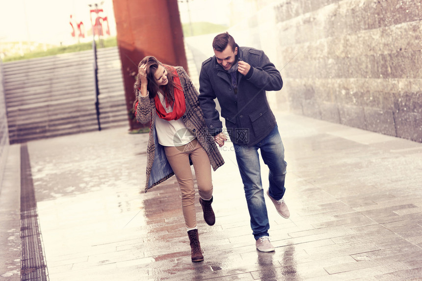 有一对年轻夫妇在雨中奔跑寻找躲雨的地方图片