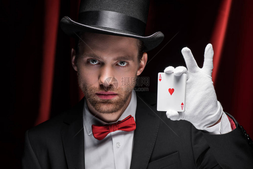魔术师在红窗帘的马戏团里拿着扑克牌图片
