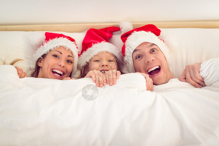 美丽的微笑家庭与圣诞老人的帽子在床上玩图片
