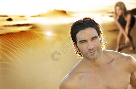 日落时在海滩上的年轻情侣关注微笑的男女在背图片