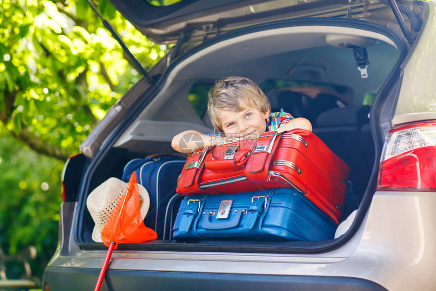 可爱的小男孩在和父母一起去暑假前坐在汽车后备箱里带着手提箱和玩具去旅行的快乐孩子快乐的家庭旅图片