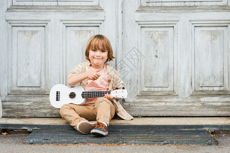 小快乐的男孩弹吉他或乌鲁勒琴坐图片