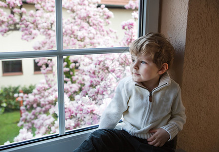 三年的小男孩望着窗外的花园图片