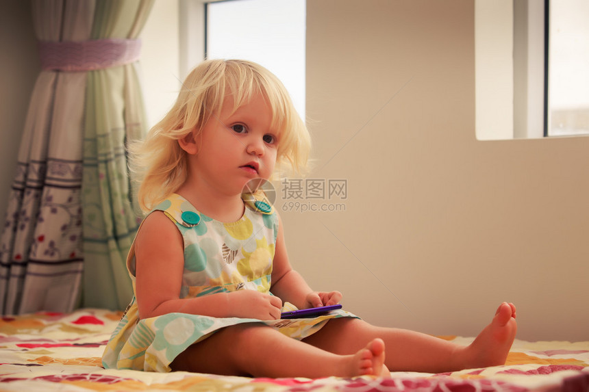 漂亮的小金发美女两岁的女孩玩智能手图片