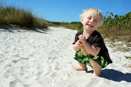 一个金发可爱的小孩蹲在沙滩上笑着图片