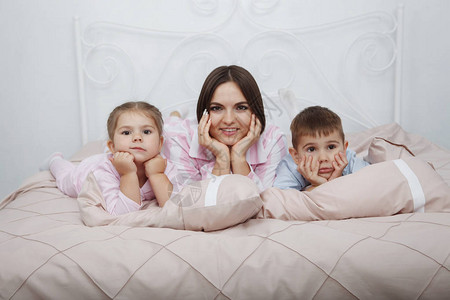 年轻漂亮的母亲与她的儿子和女儿同床睡在床上图片