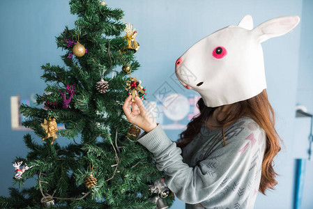 可爱的女人与有趣的兔子面具装饰小礼物盒在圣诞树上图片