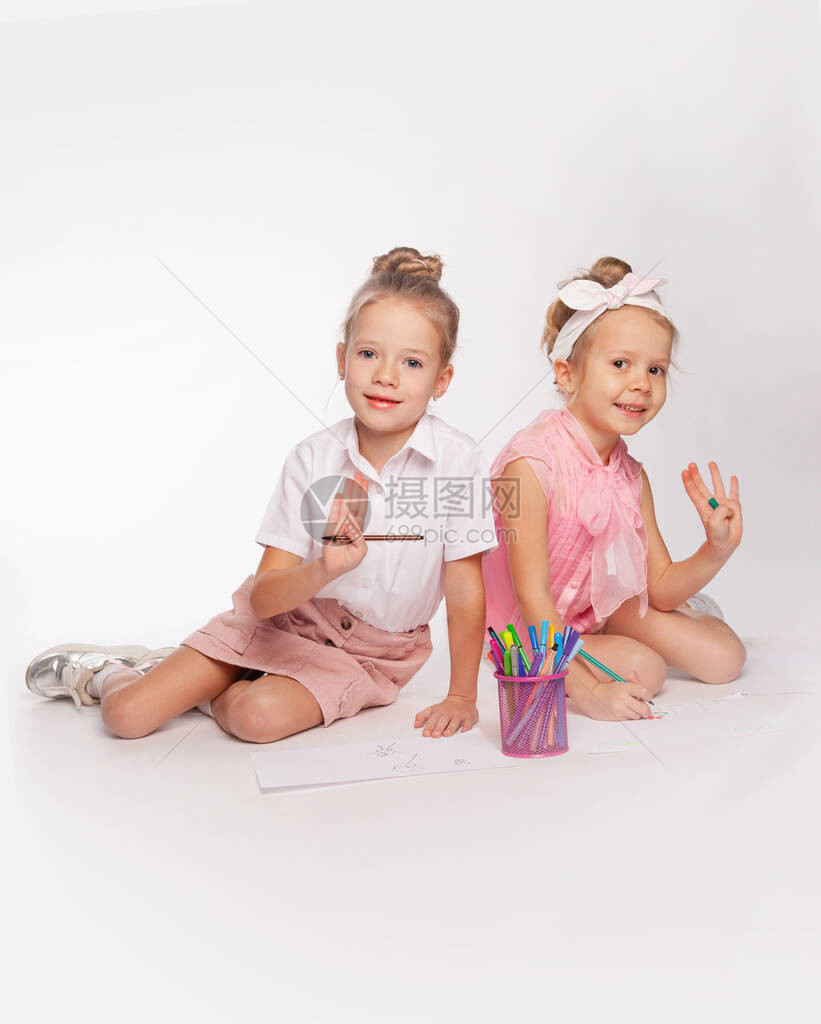两个女孩盘腿坐着用毡尖笔在纸上画图片