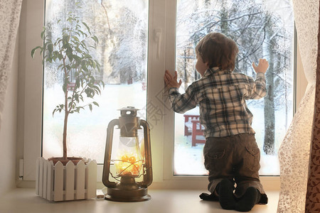小男孩坐在白色窗边看着冬天风景的窗图片