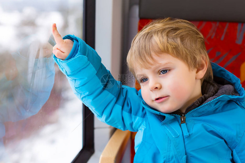 快乐可爱的蹒跚学步的小男孩从火车的窗户向外望去图片