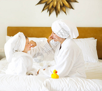 带奶油面罩的浴袍中快乐的母亲和女儿家庭护图片