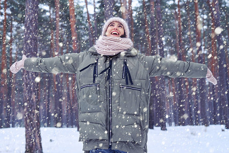 正面女士站在森林里欢喜雪和冬天的中景戴着温暖的粉红色针织帽和围巾在图片