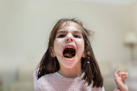 可爱的小女孩张开她的大嘴并显示咀嚼吃巧克力与笑脸图片