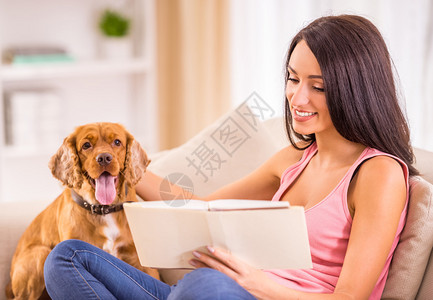 和狗狗一起坐在沙发上看书的女生图片