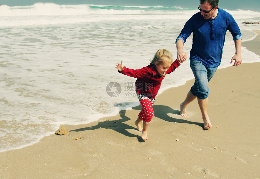 沙滩上逃离海浪的父女图片