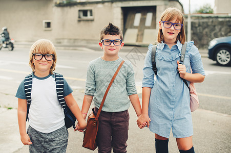 三个有趣的孩子背着包走回学校戴眼镜的女孩和男孩在路图片