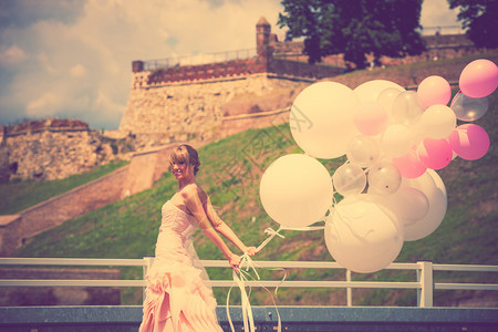 穿着优雅婚纱的快乐新娘盛放夏日户外气球复古颜色在背景中的贝图片