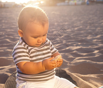 日落时可爱的婴儿坐在沙滩上看着石头图片