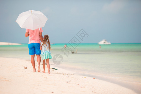 沙滩上父亲牵着女儿撑了一把遮阳伞图片