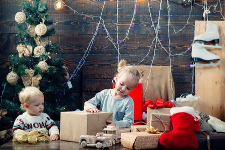 快乐的孩子在圣诞树旁看着装饰玩具球的画像戴着圣诞帽的快乐小孩带着礼物过圣诞节圣诞节快乐圣诞节前的早晨背景图片