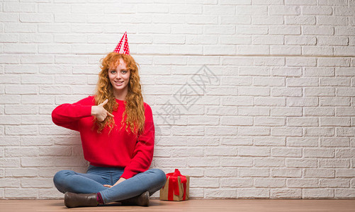 坐在砖墙上坐着戴生日帽子的年轻红发女青年图片