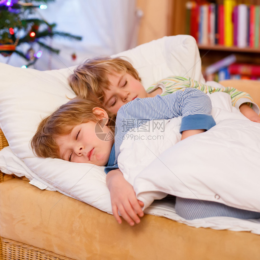 两个金发小男孩睡在圣诞树旁的床上图片