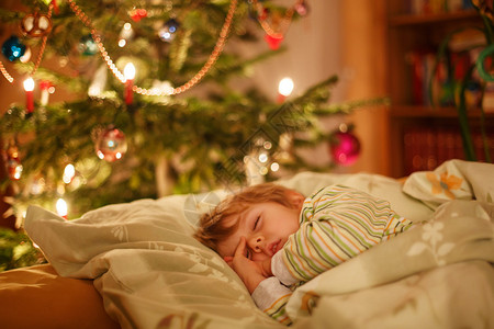 可爱的金发小男孩睡在圣诞树下在家中和室内做图片