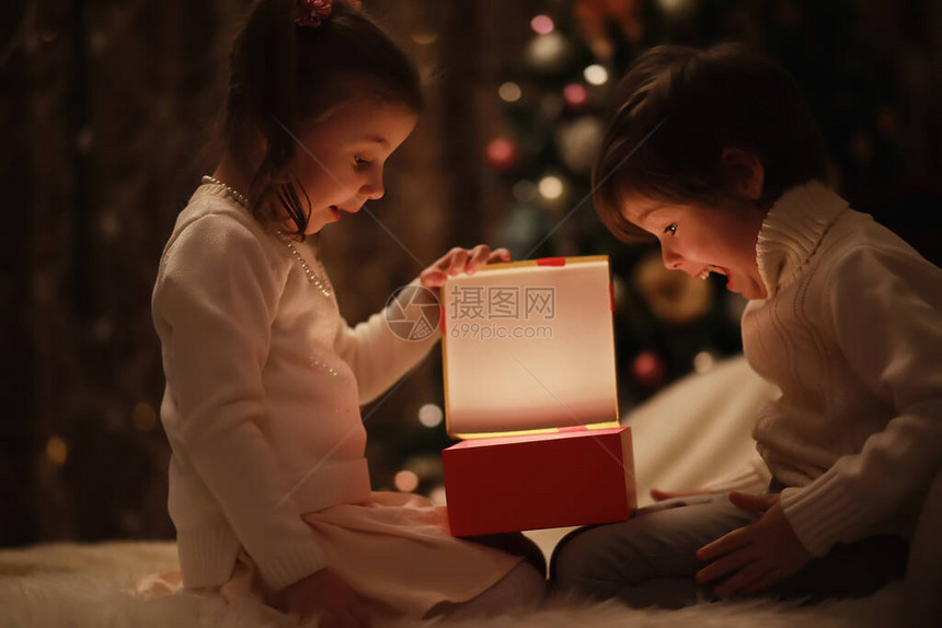 圣诞前夜在壁炉旁的孩子们打开圣诞礼物圣诞下的孩子们带着礼物盒带传统壁炉的装饰舒适温图片