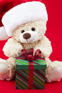 戴圣诞老人帽子的泰迪熊正坐在未开张的礼物面前图片