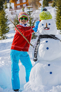 穿着红色针织北欧毛衣和温暖的帽子玩雪人的有趣快乐的女孩图片