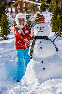 穿着红色针织北欧毛衣和温暖的帽子玩雪人的有趣快乐的女孩图片