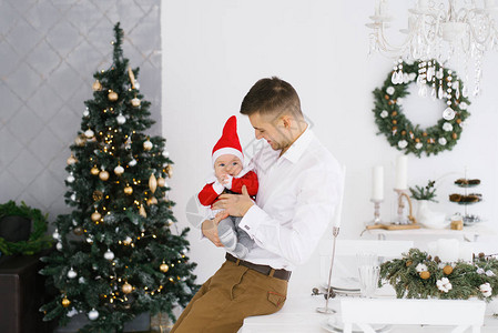年轻快乐的爸抱着他的儿子在圣诞树旁边的客厅里图片
