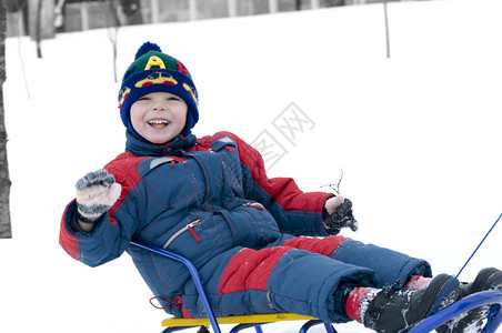 骑雪橇的男孩在雪中玩耍明亮和白图片